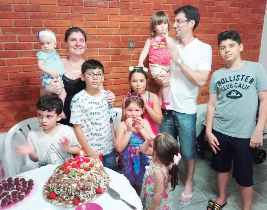 No colo do papai Rafael, a aniversariante Ana Luiza se prepara para o tradicional Parabéns e apagar as velinhas, com apoio dos primos.